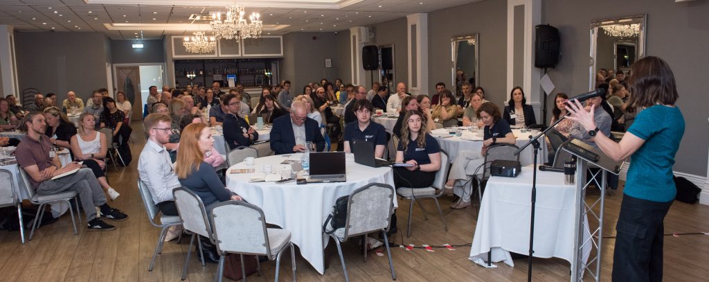 A room full of people attending the Stronger Shores Conference 2025, watching the facilitator introduce the day